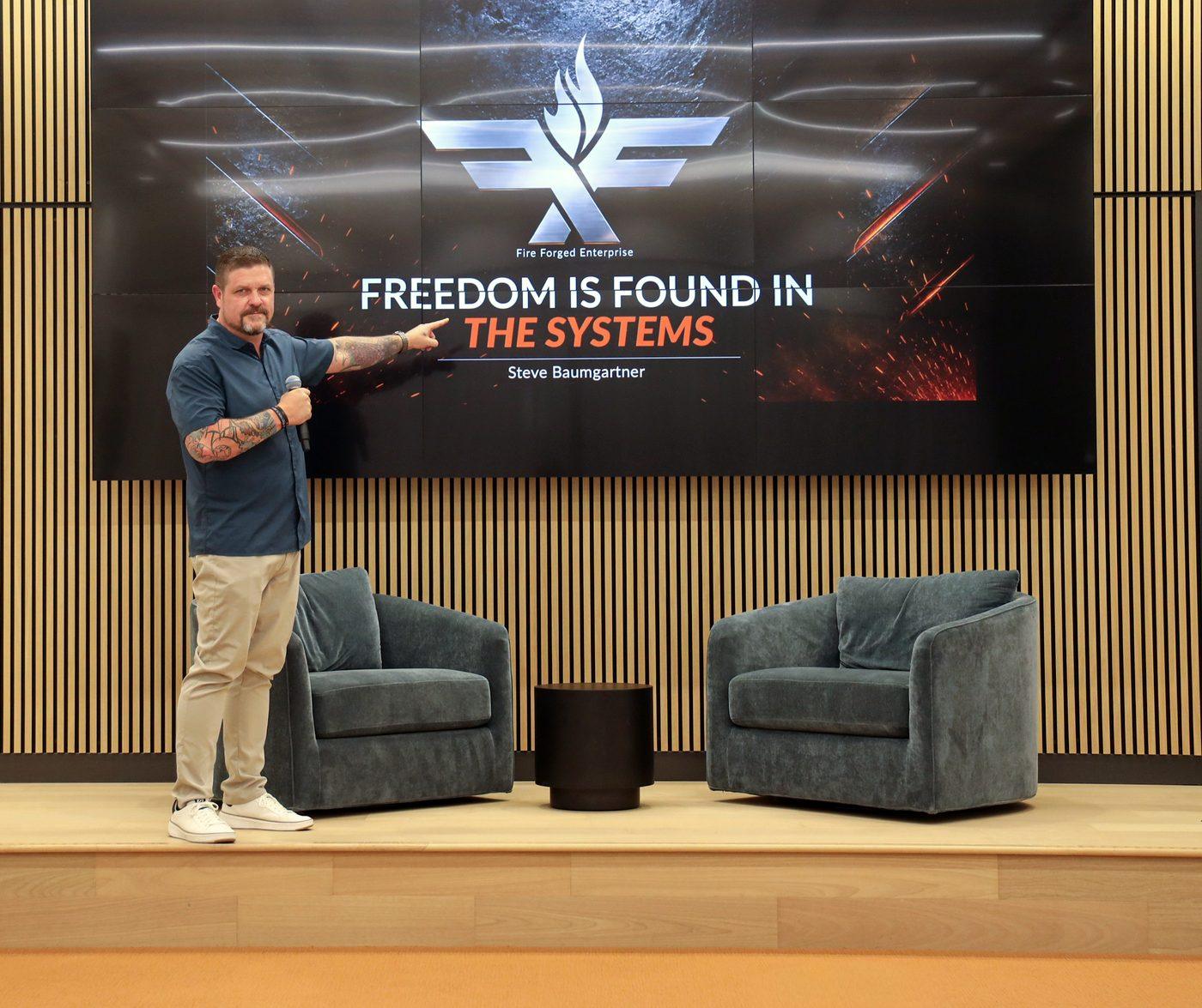 Steve pointing to a slide reading Freedom is found in the systems